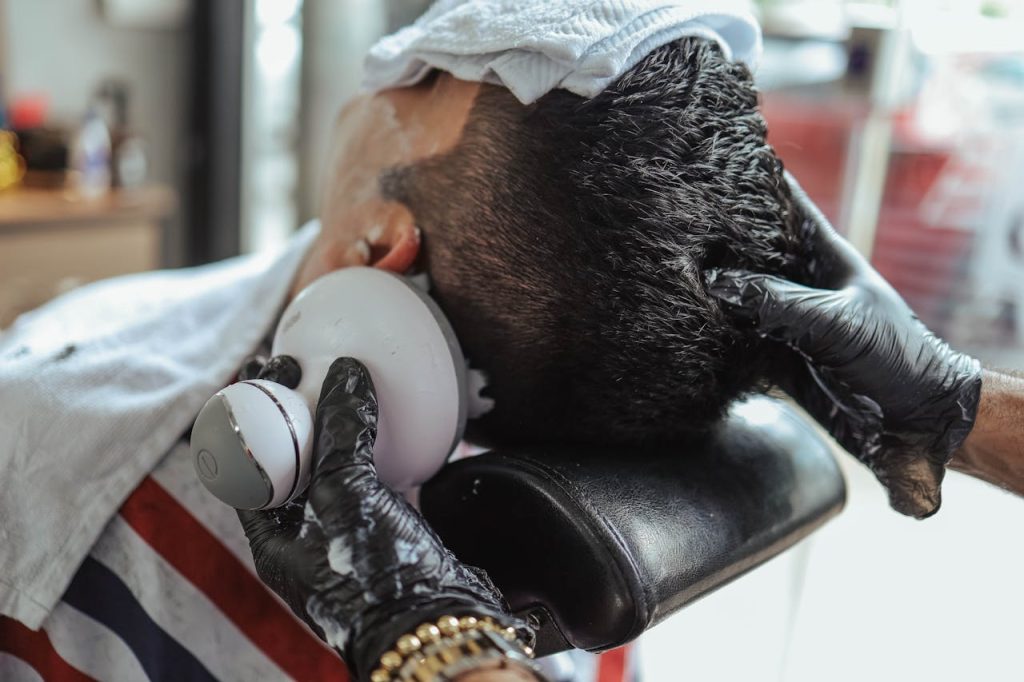 Close-up of a man receiving a haircut with an electric shaver, assisted by a hairdresser.